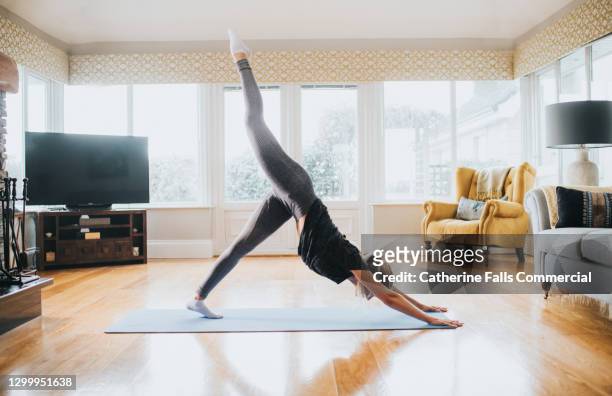 a young woman performing yoga at home on a yoga mat - downward facing dog position stock pictures, royalty-free photos & images