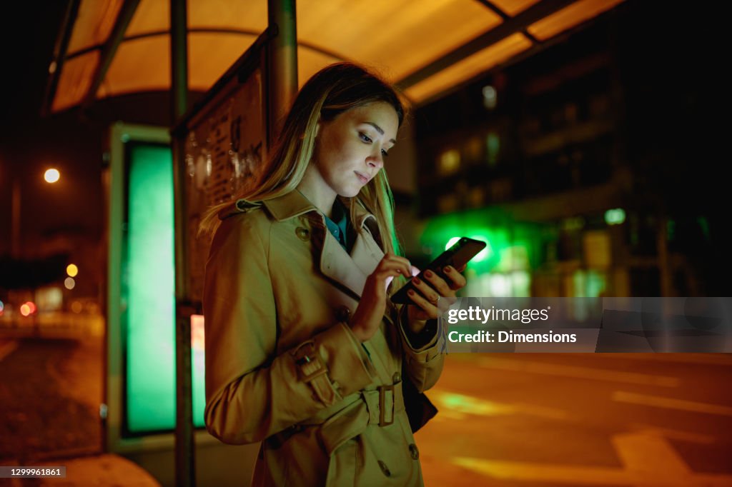 Jonge vrouw die telefoon bij de bustepost gebruikt
