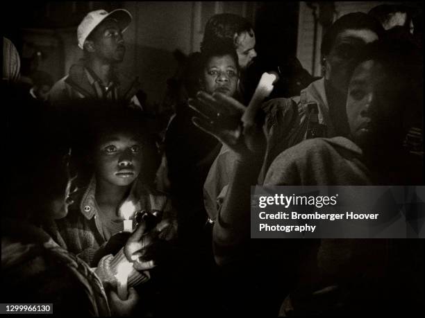 View of a people, including a young boy, gather for a candlelight vigil in the wake of Huey Newton's assassination, Oakland, California, August 22,...