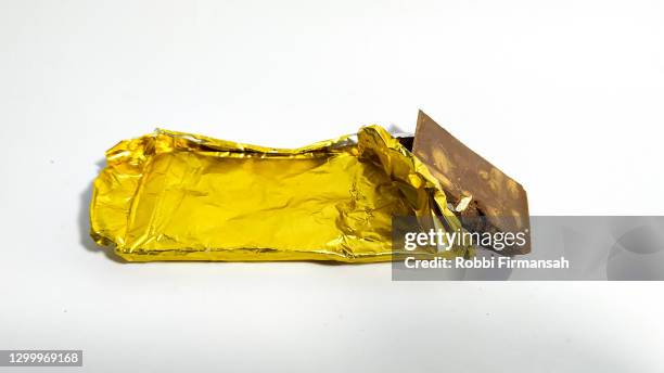 chocolate bar in yellow packaging and pieces on white background - chocolate foil stock-fotos und bilder