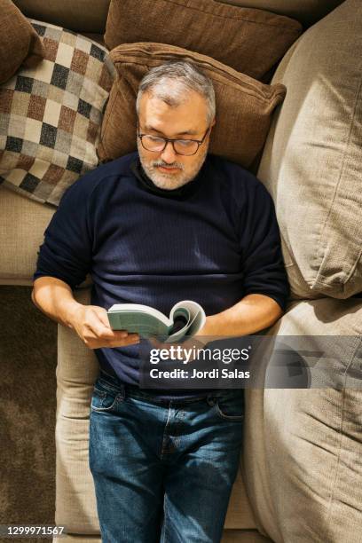 man reading a book on the sofa - südeuropäischer abstammung stock-fotos und bilder