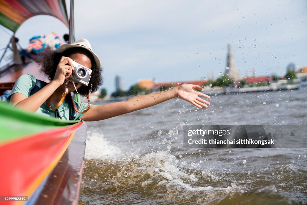 Female tourist on longtail boat joy view and take photo Wat Arun at morning, Chao Phraya river, Bangkok Thailand