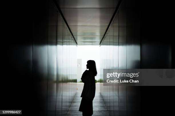 silhouette der asiatischen frau steht gegen dunklen korridor in einem park - dark room stock-fotos und bilder