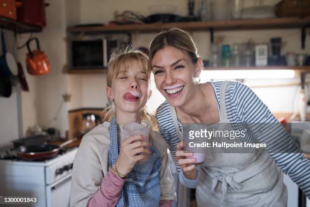 mother and small daughter indoors in kitchen, drinking milkshake drink. - milk family stock pictures, royalty-free photos & images