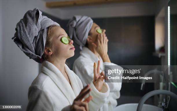mother and small daughter indoors in bathroom at home, putting cucumbers on eyes. - se faire dorloter photos et images de collection