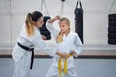 Teenage girl in kimono practicing karate with a instructor in a sports gym. Martial arts training session