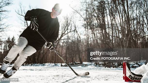 mature man playing hockey outdoors - outdoor ice hockey stock pictures, royalty-free photos & images