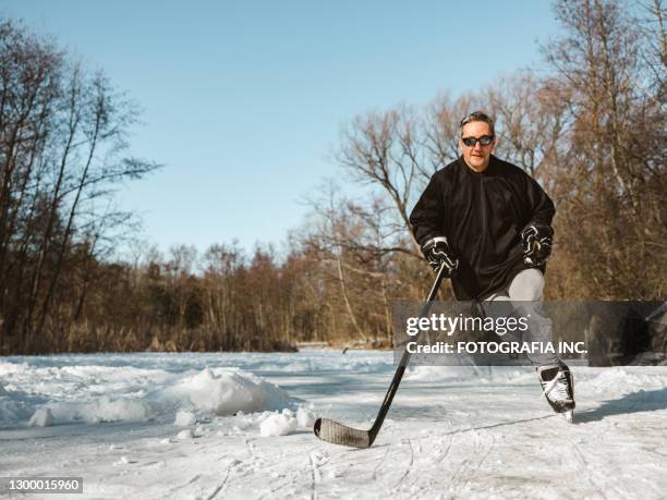 mature man playing hockey outdoors - pond hockey stock pictures, royalty-free photos & images