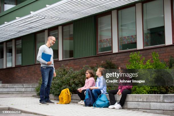 teacher talking to schoolchildren in front of school - school yard stock pictures, royalty-free photos & images