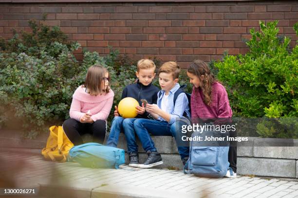 children looking at cell phone in front of school building - teaching remotely stock pictures, royalty-free photos & images