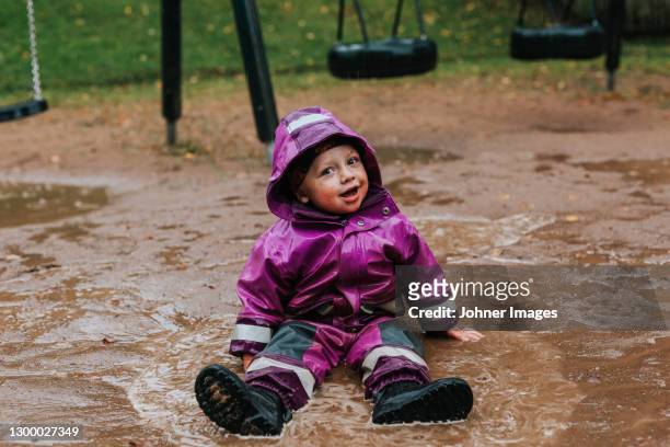 toddler girl sitting in puddle - pfütze stock-fotos und bilder