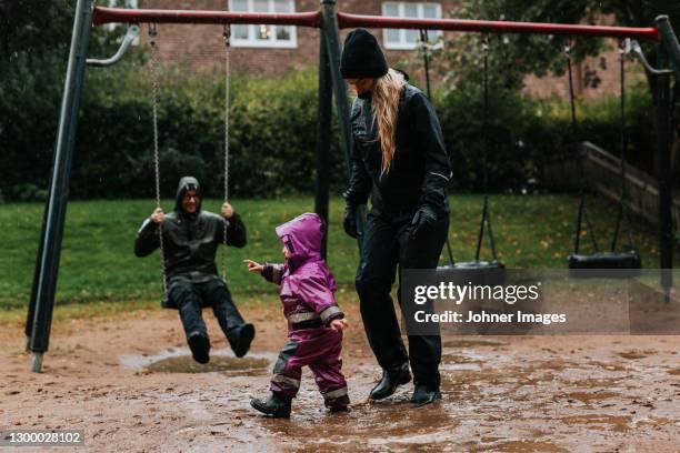 parents with toddler on playground - schaukel regen stock-fotos und bilder