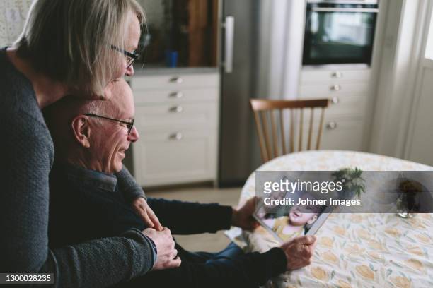 smiling couple having video chat with baby grandson on tablet - 3 women senior kitchen stock pictures, royalty-free photos & images