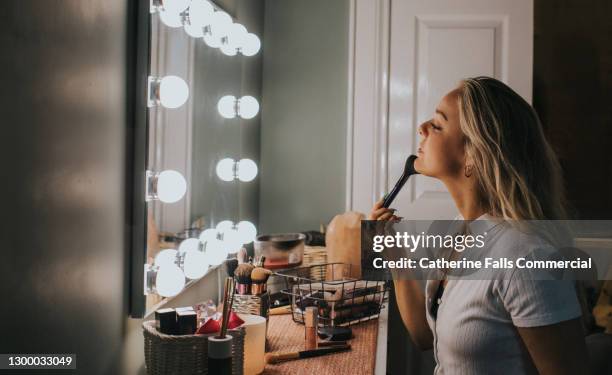 a young woman applies powder foundation in an illuminated mirror - bedroom vanity stock pictures, royalty-free photos & images