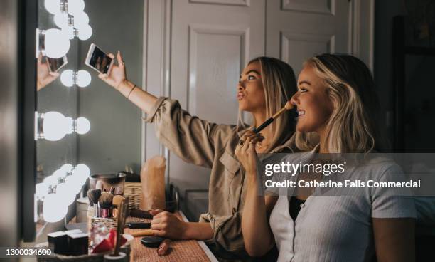 two young woman sit infront of a illuminated mirror and take a selfie - preocupación por el cuerpo fotografías e imágenes de stock