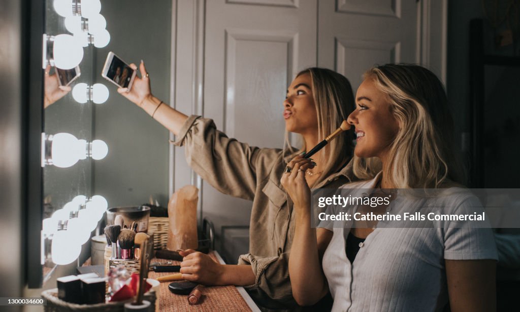 Two young woman sit infront of a illuminated mirror and take a selfie