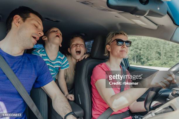 happy mother drives a car while traveling with her husband and kids yawning and falling asleep - yawning mother child stock pictures, royalty-free photos & images
