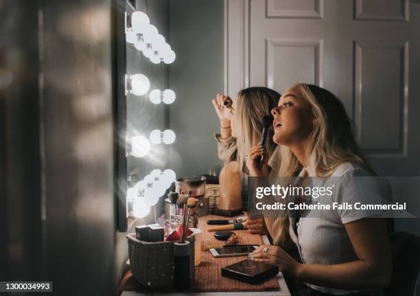 two woman concentrate as they apply make-up in an illuminated mirror - dressing table stock pictures, royalty-free photos & images
