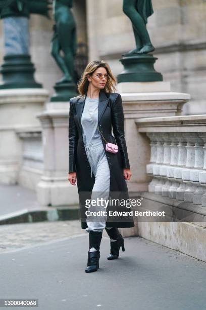 Natalia Verza aka Mascarada wears small circular sunglasses, a black leather long coat with shoulder pads from Fendi, a gray t-shirt, gray sport...