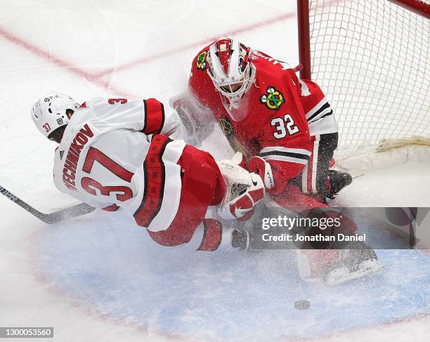 Kevin Lankinen of the Chicago Blackhawks makes a save against Andrei Svechnikov of the Carolina Hurricanes as Svechnikov slips and crashes into him...