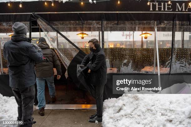 Maître d'hôtel opens a plastic tarp for customers at The Mark's enclosed outdoor dining structure near piles of snow on February 02, 2021 in New York...