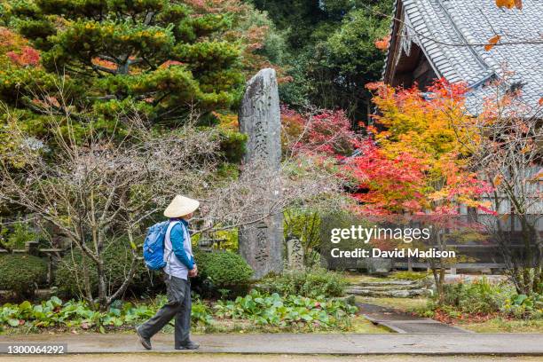 Pilgrim or "henro" wearing traditional conical hat and white garment walks on the grounds of Sankaku-ji, Temple 65 of the Shikoku 88 Buddhist temple...