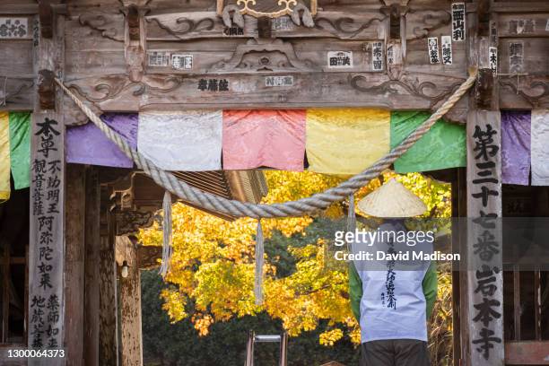 Pilgrim, or "henro", wearing traditional conical hat and white vest, stands at the entrance gate of Iwamoto-ji, Temple 37 of the Shikoku 88 Buddhist...