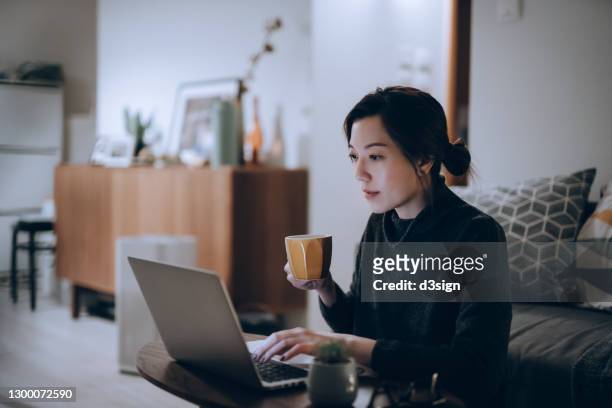 busy concentrated young asian woman working from home, working on laptop till late in the evening at home. home office, overworked, deadline and lifestyle concept - leanincollection working women stockfoto's en -beelden