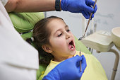Brave child sitting at the dentist’s chair while the female dentis using dentist’s probe for scrutinity