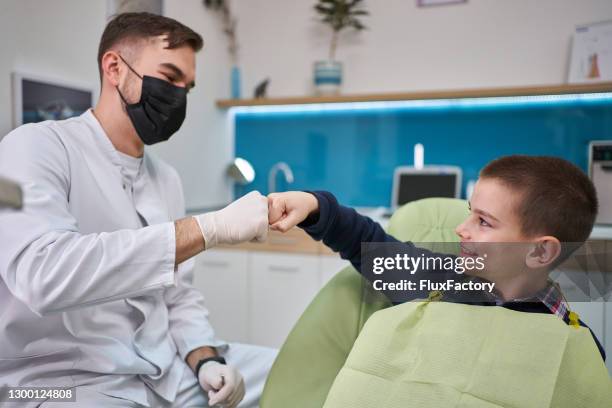 coraggioso pugno ragazzo urtare il suo dentista dopo una procedura dentale di successo - dentista bambini foto e immagini stock
