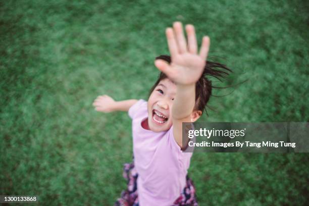 lovely little girl reaching one hand toward sky while playing joyfully on the lawn in park - ein tag im leben stock-fotos und bilder