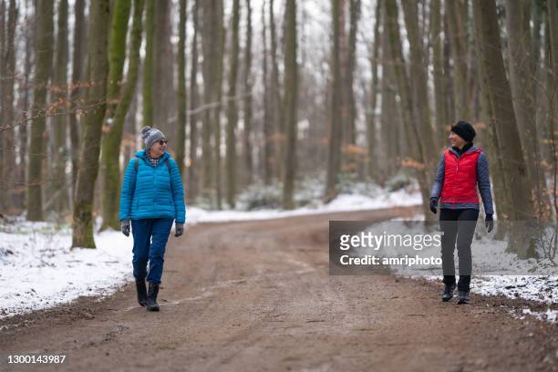 twee gelukkige vrouw van verschillende leeftijd die langs het registreren weg door bos in de winter loopt die juiste afstand houdt - social distancing stockfoto's en -beelden