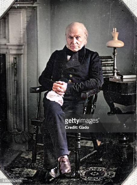 Full length portrait of American president John Quincy Adams from a Daguerreotype, seated in a chair with hands clasped, with rug and lamp visible,...