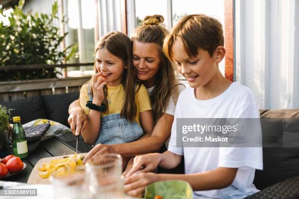 smiling mother cutting vegetable on table in balcony - familie eten stockfoto's en -beelden