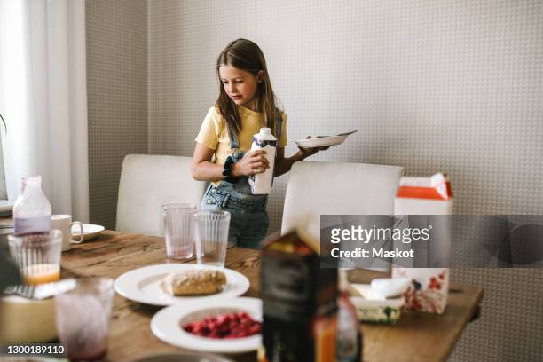 pre-adolescent girl with plate and juice pack standing by dining table - juice carton 個照片及圖片檔