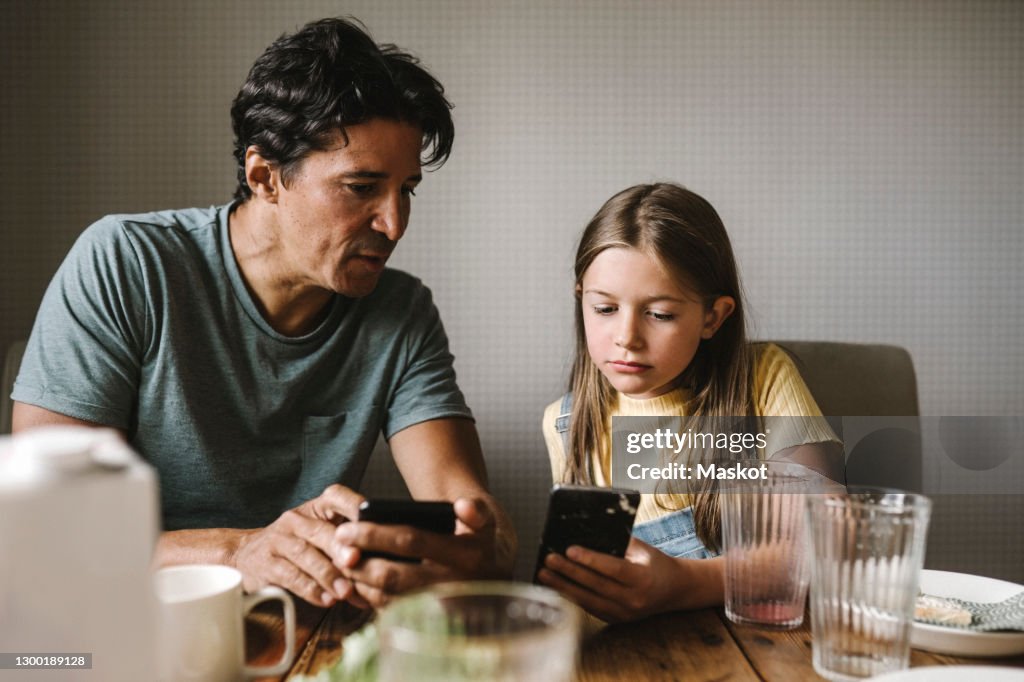 Daughter and father using smart phone over dining table at home