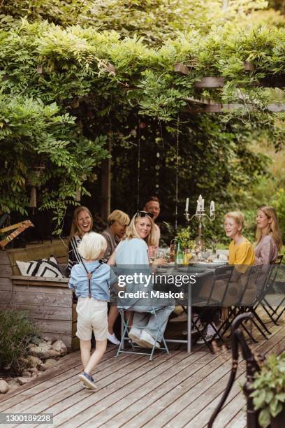 smiling family looking at boy walking during dinner party in back yard - backyard deck stock pictures, royalty-free photos & images