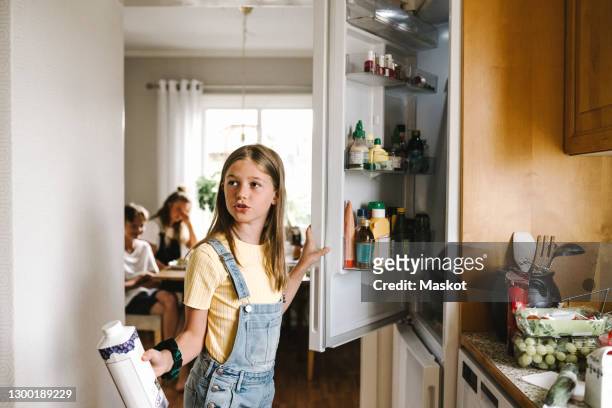 caucasian girl with juice pack standing by refrigerator - refrigerator stock-fotos und bilder
