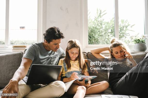 daughter doing homework sitting by mother and father in living room - telecommunicatie apparatuur stockfoto's en -beelden