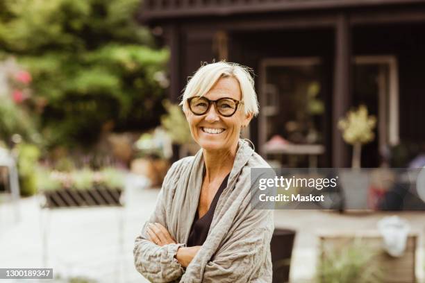 smiling mature woman with arms crossed in back yard - 55 59 jaar stockfoto's en -beelden