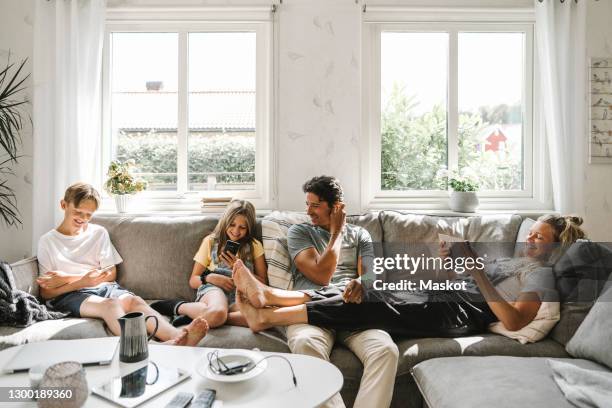 happy family sitting on sofa in living room - woman smartphone family ストックフォトと画像
