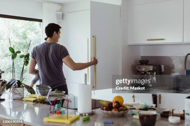 father opening refrigerator while carrying baby son in kitchen - open day 1 stockfoto's en -beelden