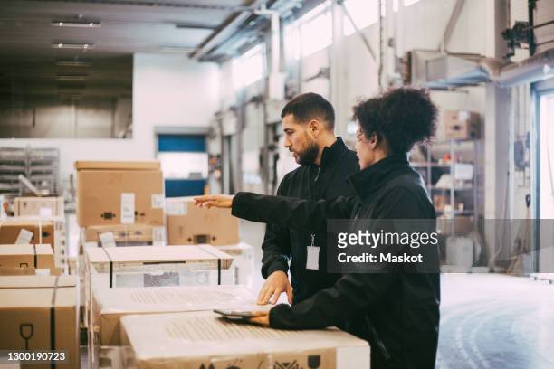 businesswoman pointing while discussing with male colleague at warehouse - distribution warehouse stockfoto's en -beelden