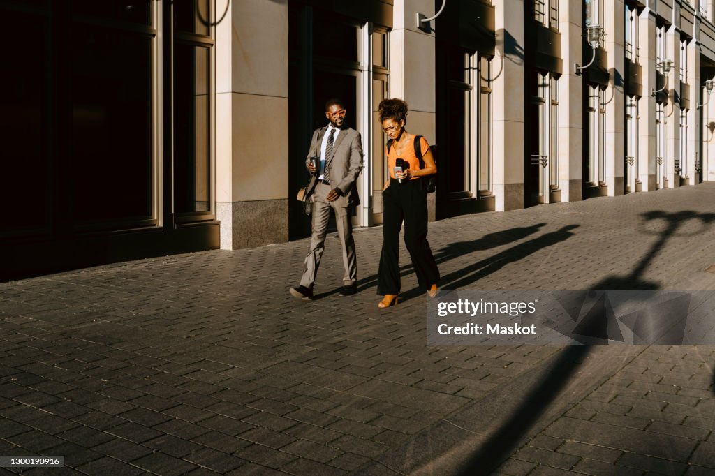 Male and female coworkers discussing while walking on footpath during sunny day