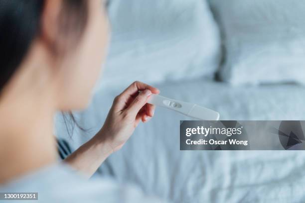 rear view cropped shot of woman holding home pregnancy test in bedroom - pregnancy test stock pictures, royalty-free photos & images
