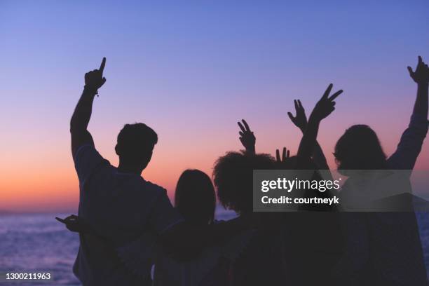 gruppe von menschen, die bei sonnenuntergang oder sonnenaufgang am strand feiern. - sunset party stock-fotos und bilder