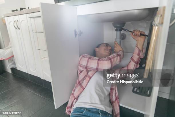 vrouw thuis in de keuken die een lekprobleem in de gootsteen probeert op te lossen - broken pipe stockfoto's en -beelden