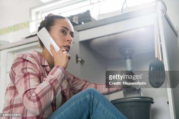 mujer en casa llamando a un fontanero sobre una tubería con fugas en su fregadero - seguro del hogar fotografías e imágenes de stock