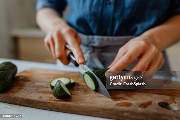 mains d’une femme coupant des concombres sur une planche à découper - coupant photos et images de collection