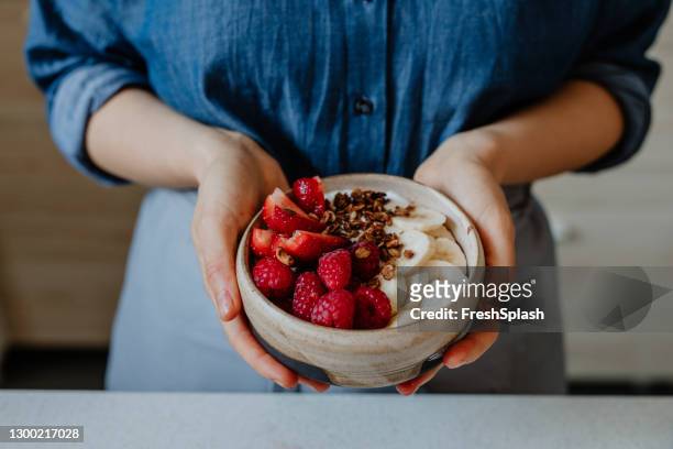 healthy and nutritious breakfast: anonymous woman holding a bowl of delicious oatmeal with fruit and greek yoghurt - muesli stock pictures, royalty-free photos & images